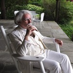mark dawidziak in a white suit dressed as mark twain sitting in a rocking chair on an outside porch